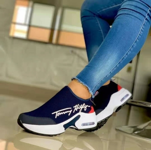 A pair of Tommy Hilfiger slip-on sneakers displayed on a person's feet wearing blue jeans.ELITE CASA Breathable Women’s Wedge Sneakers